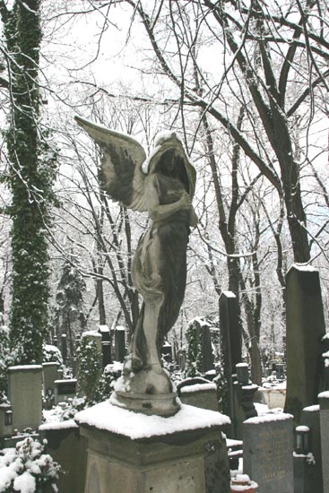 A snowy angel stands on the headstone of a grave in a cemetary in Prague.